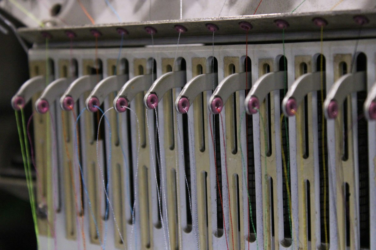 Close-up of an industrial embroidery machine's thread guides — precision stitching in progress